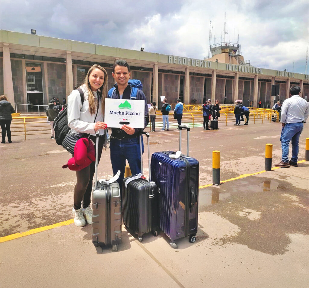 Turistas son recibidos en el aeropuerto de Cusco con un cartel de bienvenida, representando el acompañamiento personalizado desde el inicio de tu viaje en Perú