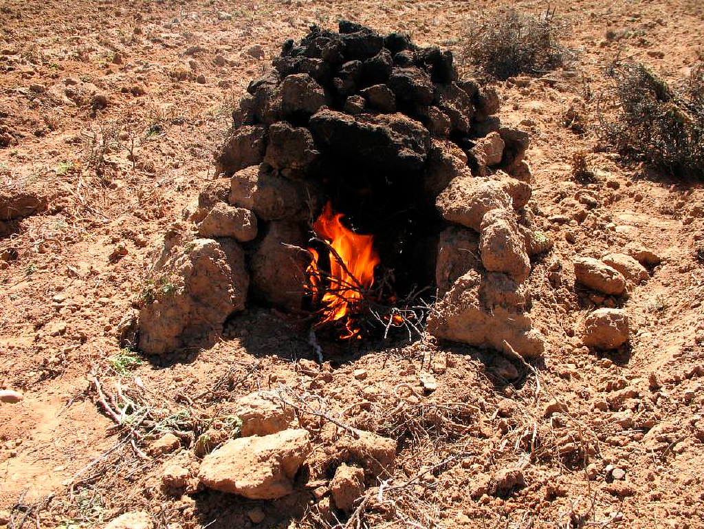Estructura de huatia con terrones de tierra y fuego encendido en su interior, lista para la cocción de alimentos andinos