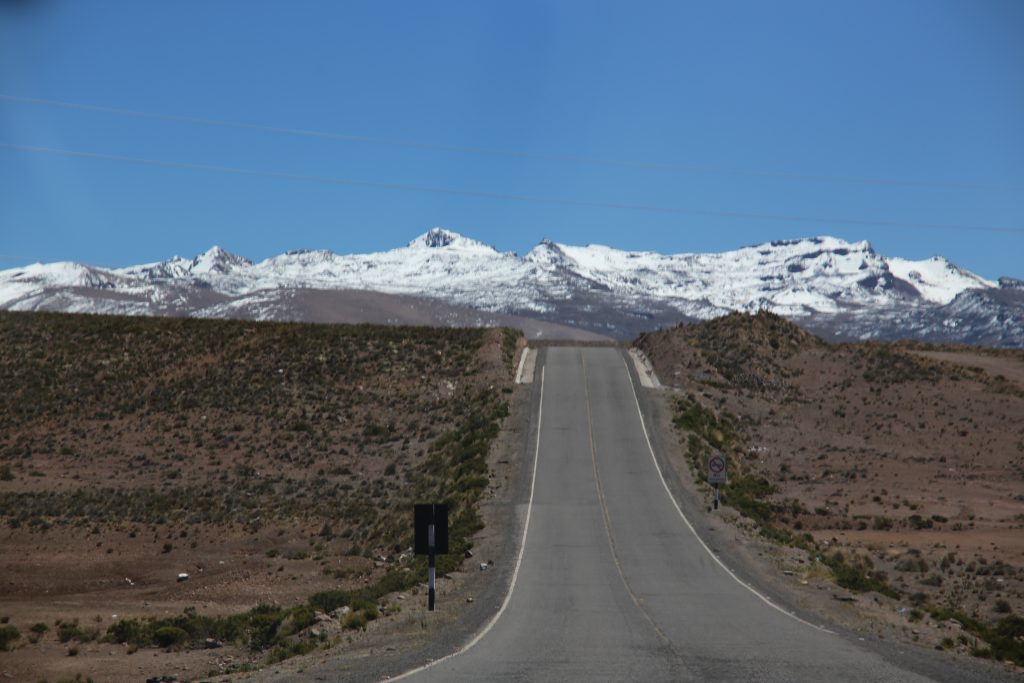 Carretera solitaria en la ruta de Arequipa a Chivay, atravesando paisajes andinos remotos con nieve en las montañas al fondo