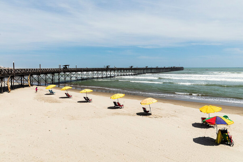Playa de Pimentel con sombrillas amarillas y muelle de madera al fondo, en la costa norte de Lambayeque, Perú