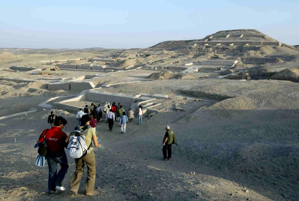 Grupo de visitantes recorriendo el sitio arqueológico de Cahuachi, rodeado de estructuras ceremoniales de adobe en el desierto de Nazca.