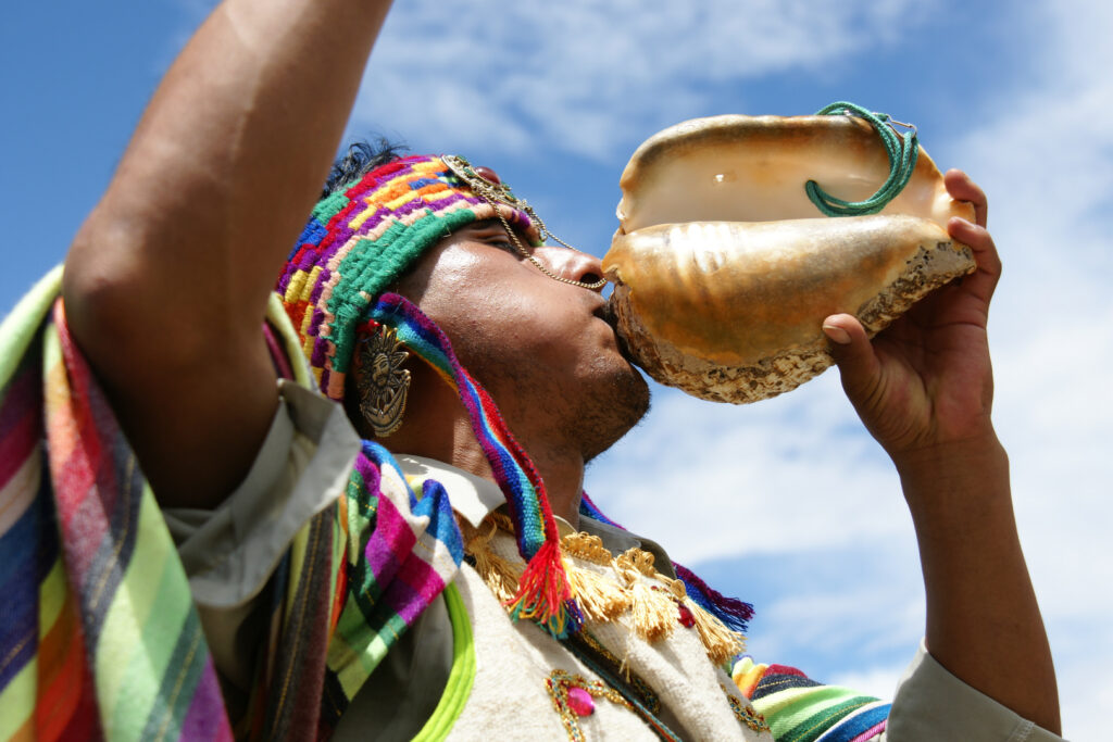 Guía espiritual andino tocando un pututo como parte de un ritual ceremonial