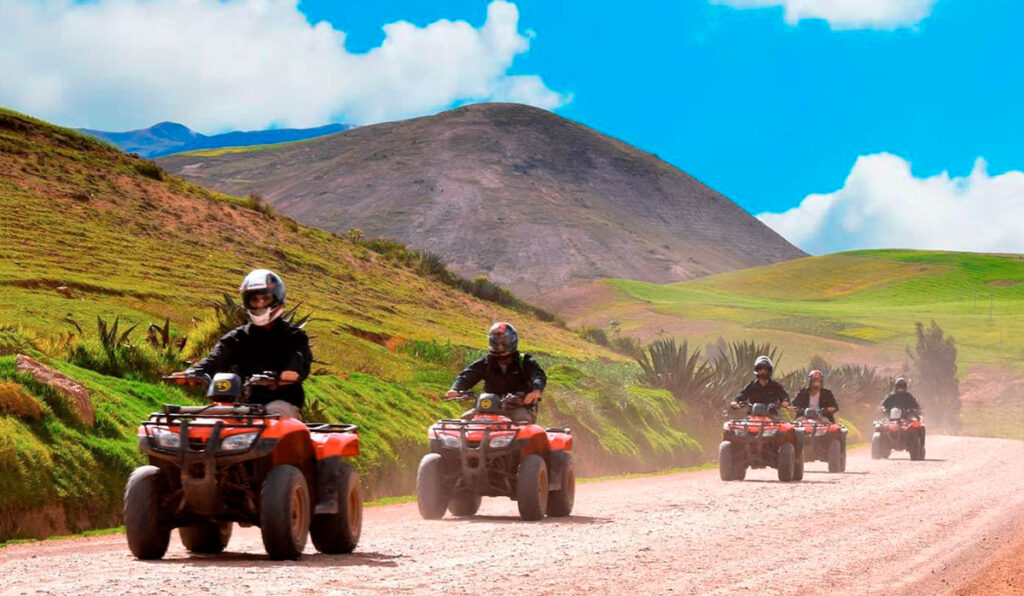 Turistas recorriendo en cuatrimoto los caminos andinos de Maras, Cusco, rodeados de montañas y campos verdes