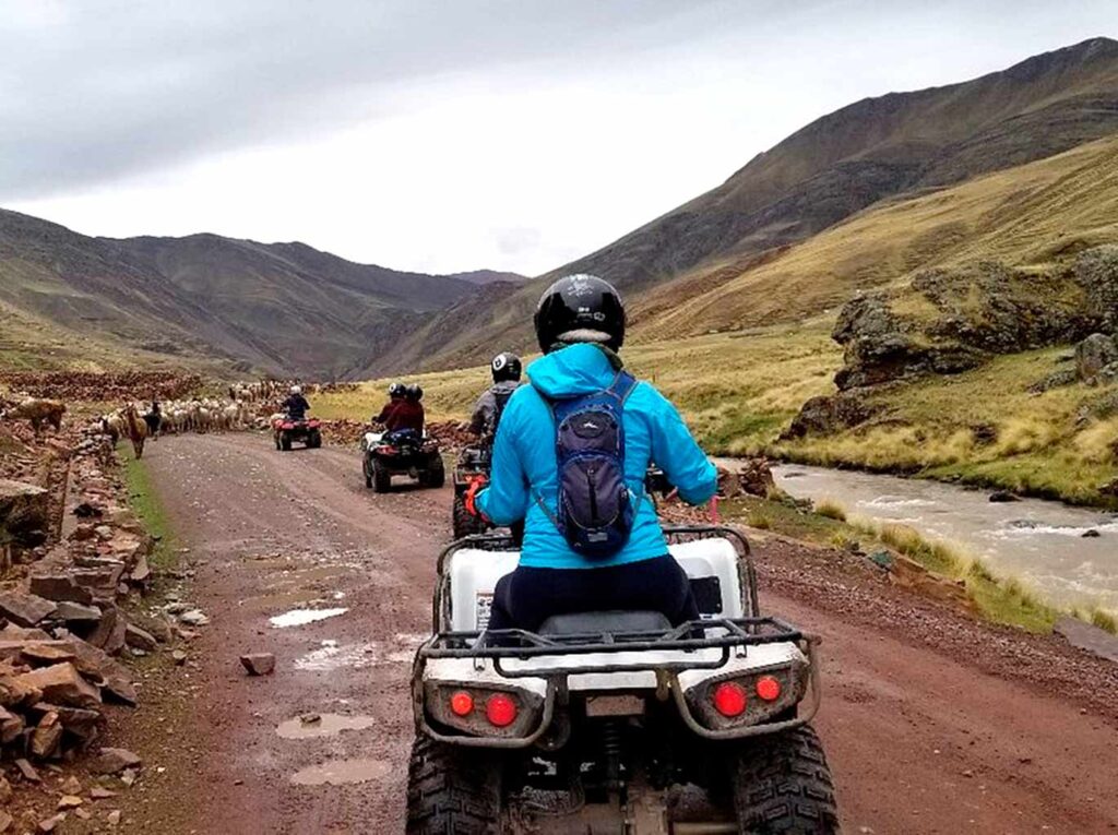 Grupo de turistas en cuatrimoto rumbo a Vinicunca por caminos rurales del altiplano, rodeados de montañas y llamas