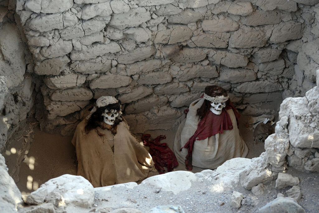 Momias sentadas en una tumba restaurada del cementerio de Chauchilla, envueltas en fardos funerarios nazca y resguardadas por muros de adobe