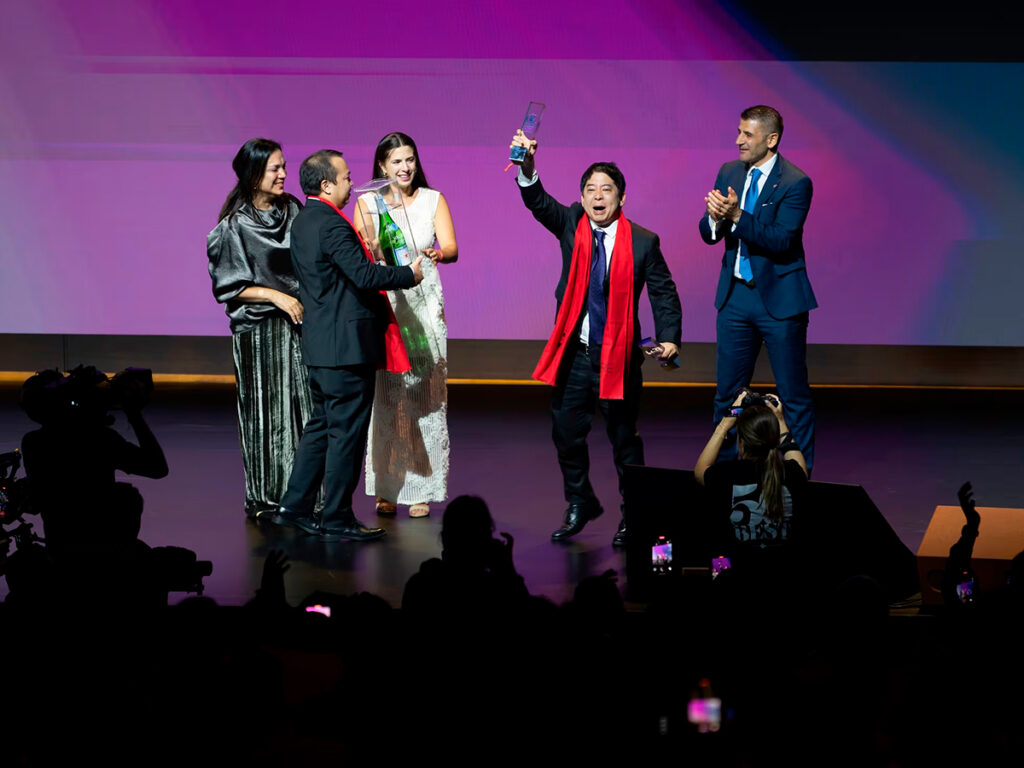 Mitsuharu Tsumura levanta el trofeo de Maido como mejor restaurante del mundo 2025 durante la ceremonia de premiación, rodeado de colegas en el escenario