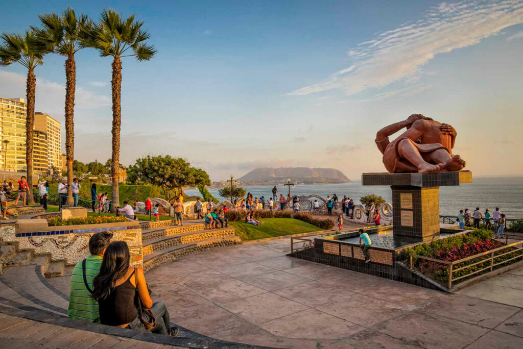 Vista del Parque del Amor en el Malecón de Miraflores al atardecer, con la escultura “El Beso” y visitantes frente al mar