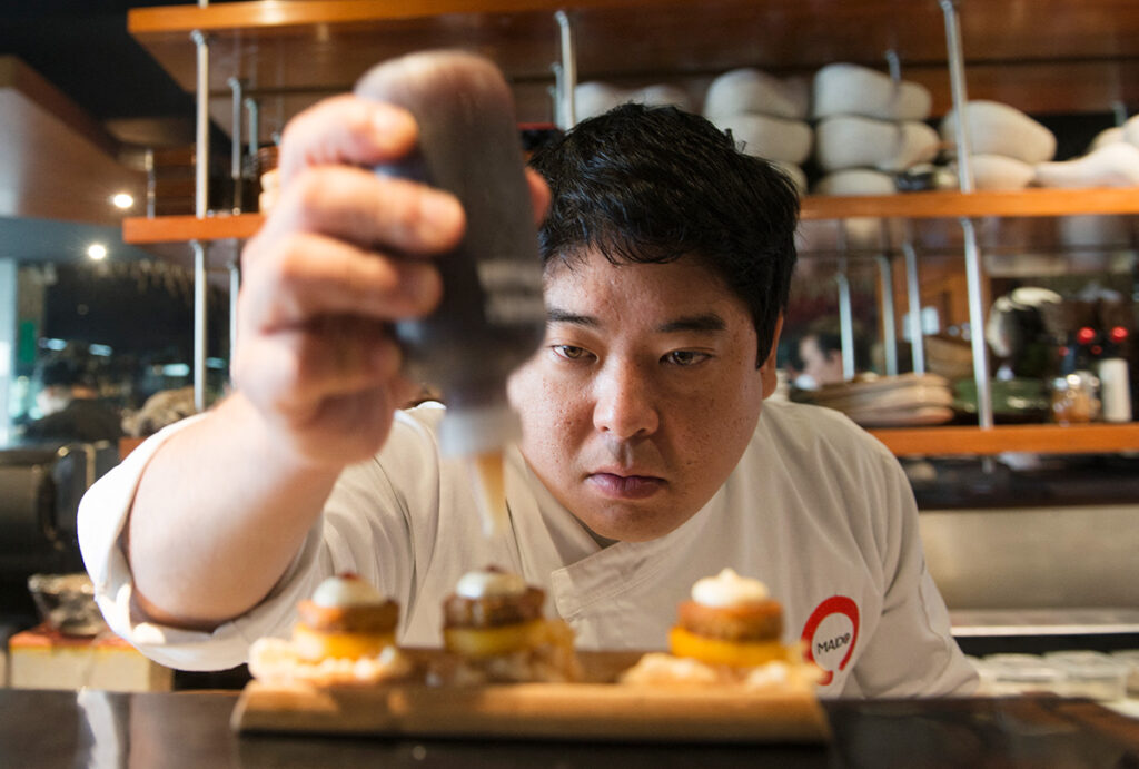 Mitsuharu Tsumura concentrado mientras aplica detalles a un plato en la cocina de Maido