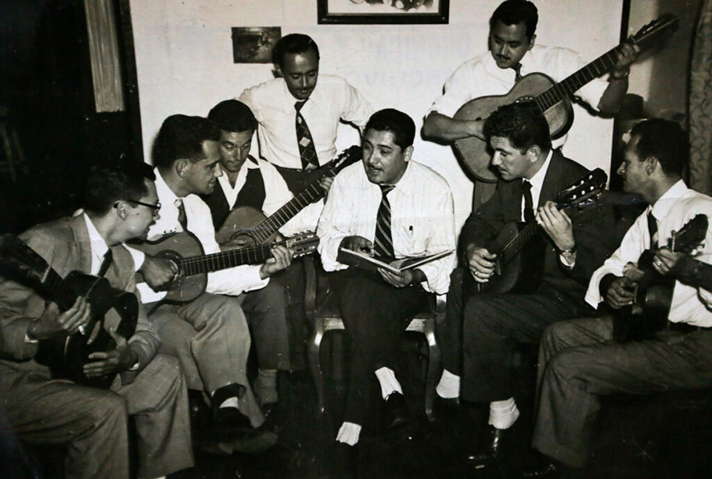 Óscar Avilés en blanco y negro, tocando guitarra junto a un grupo de músicos criollos en un ensayo tradicional en Lima
