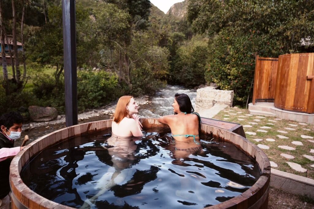 Dos mujeres disfrutando de una tina de agua caliente al aire libre en un hotel ecológico de Ollantaytambo, rodeadas de naturaleza andina