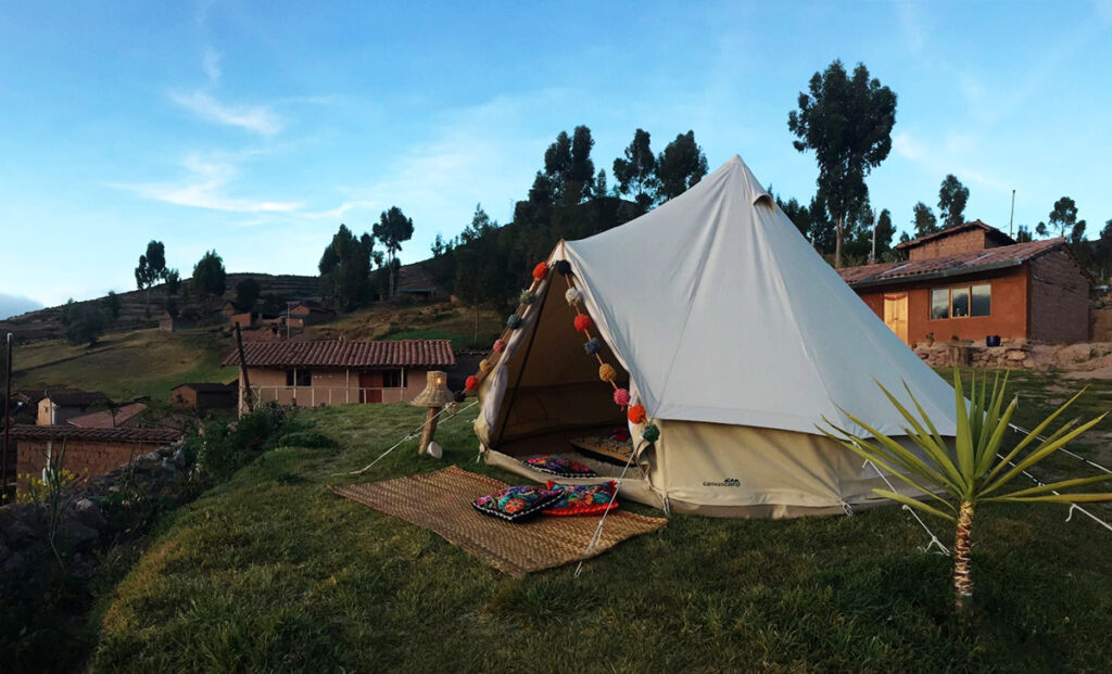 Carpa de glamping decorada con textiles andinos en el Qhispikay Sustainable Lodge, rodeada de campos y casas rurales en la comunidad de Misminay