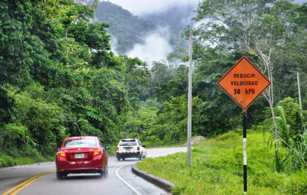 Carretera rodeada de vegetación en la ruta de Tarapoto hacia la catarata de Ahuashiyacu, con señal de tránsito visible