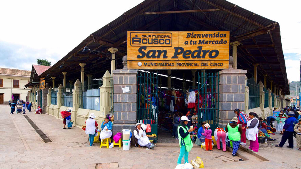 Vista frontal del Mercado Central de San Pedro en Cusco, con visitantes y vendedoras locales en la entrada durante una mañana festiva