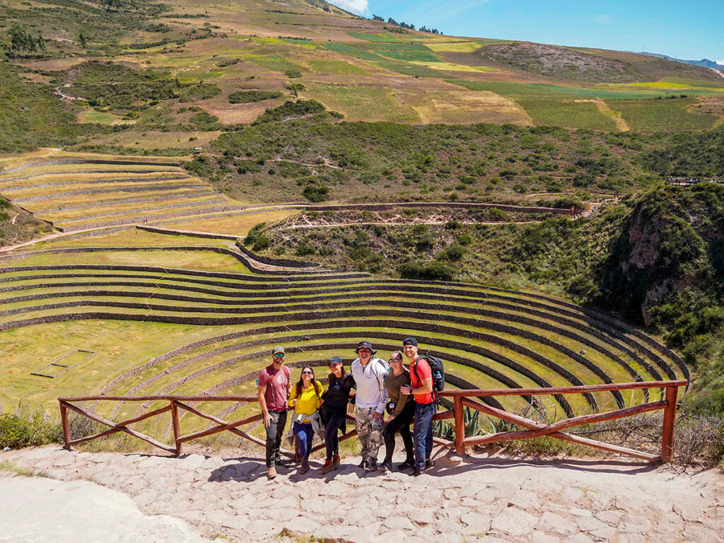 Grupo de turistas frente a las terrazas agrícolas de Moray, integradas armónicamente al paisaje natural del Valle Sagrado.