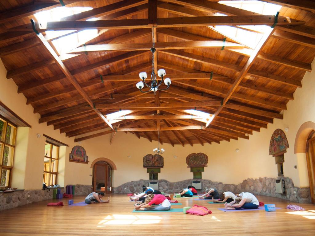 Personas practicando yoga en un salón de madera con techo alto, en un centro de retiro espiritual en Pisac, Valle Sagrado del Cusco