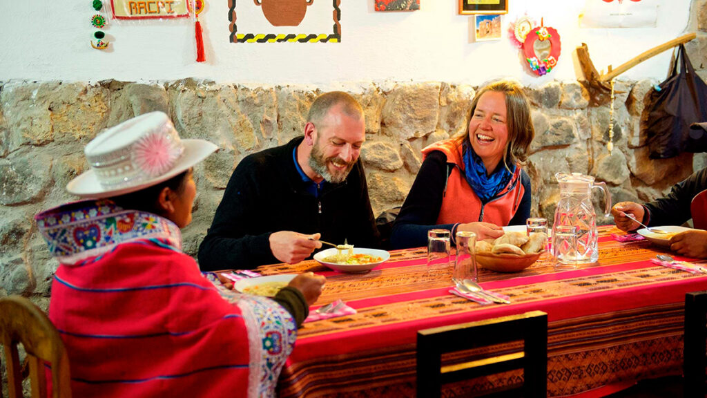 Turistas compartiendo una comida típica con familias locales en Coporaque, Valle del Colca