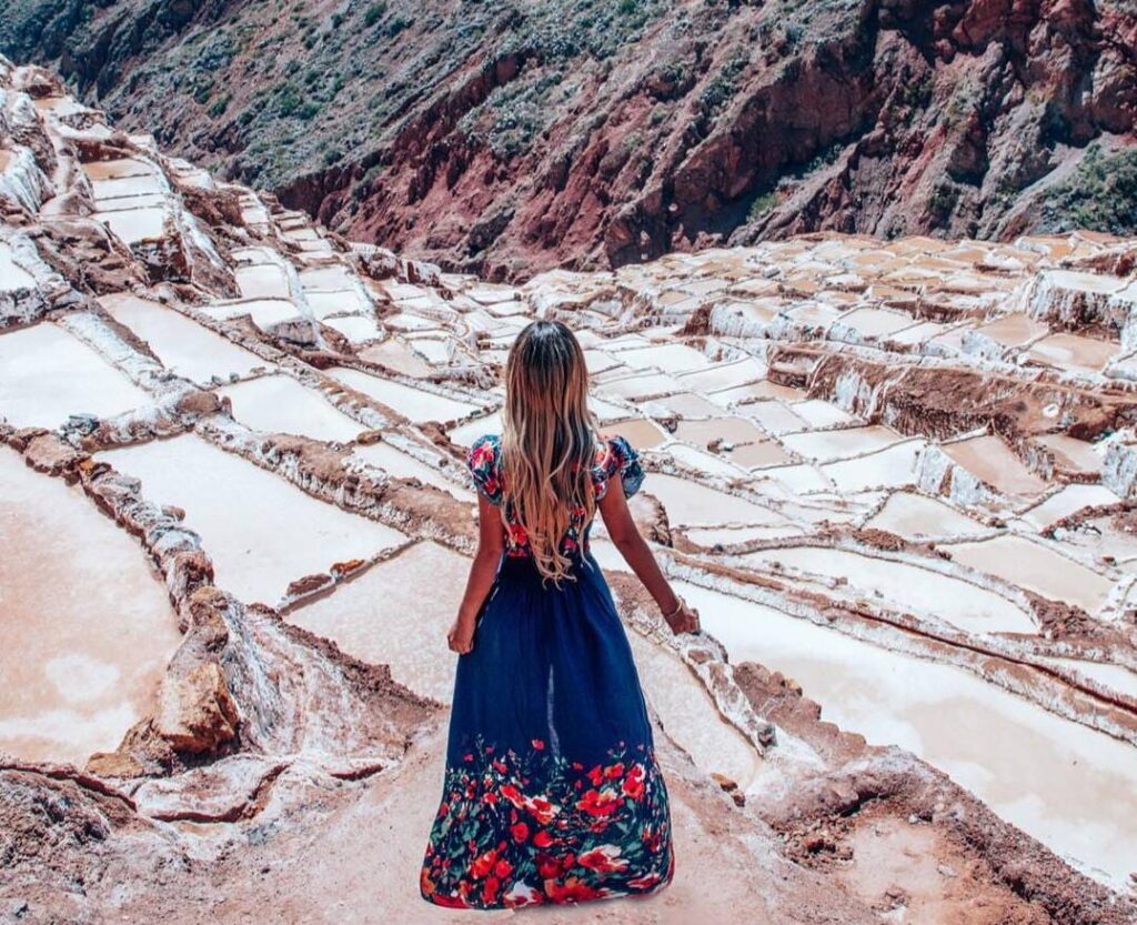 Mujer de espaldas observando las Salineras de Maras desde una pasarela entre las pozas blancas