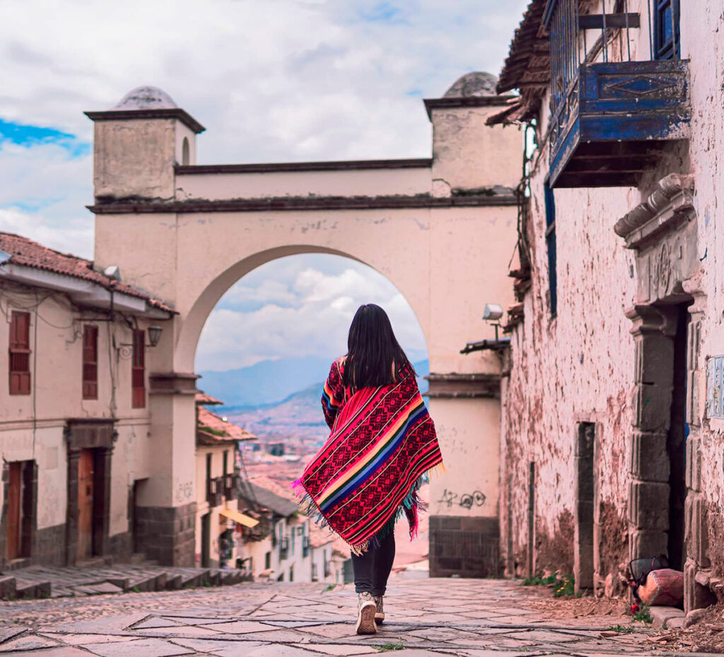 Mujer vestida con un poncho típico, caminando hacia el Arco de Santa Ana en Cusco por la empinada Cuesta de Santa Ana