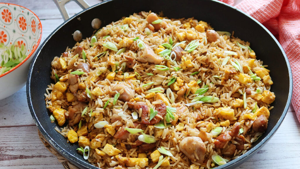 Plato de arroz chaufa servido en sartén, con pollo, tortilla de huevo, cebolla china y sillao