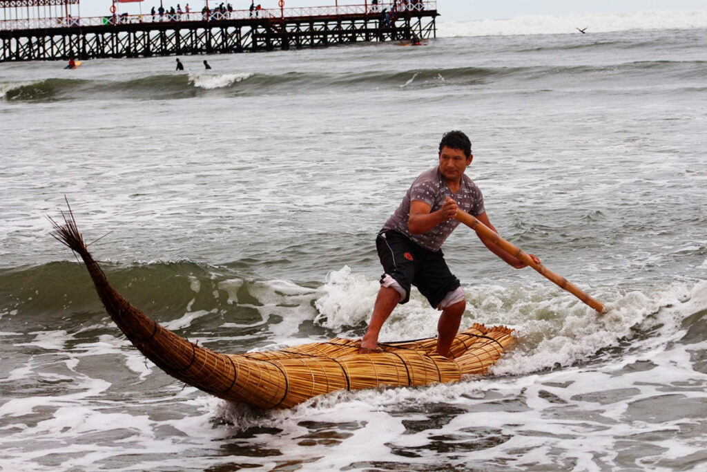 Pescador de Huanchaco navegando sobre un caballito de totora frente al muelle
