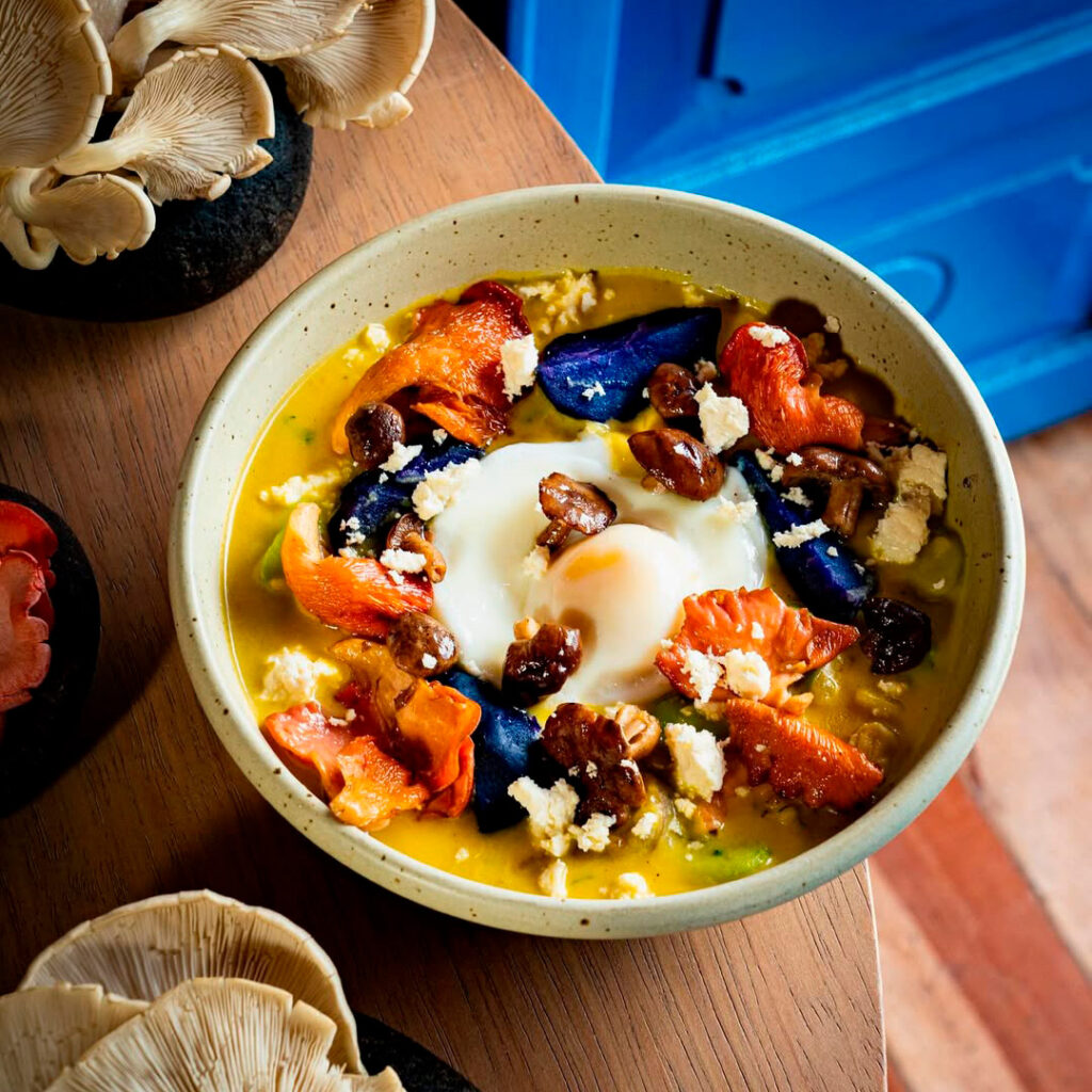 Plato gourmet servido en Chicha por Gastón Acurio, con una base cremosa, vegetales coloridos, queso fresco y frutos secos, presentado en vajilla artesanal