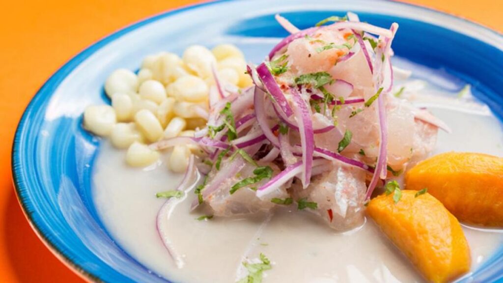 Ceviche servido al instante con camote, choclo y cebolla morada sobre un plato azul