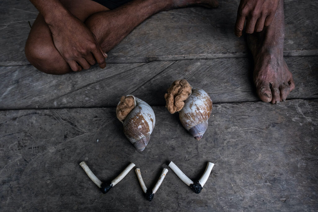 Elementos rituales machiguengas dispuestos sobre el suelo: caracoles, tabaco mapacho y pies descalzos que evocan el vínculo entre cuerpo, espíritu y tierra