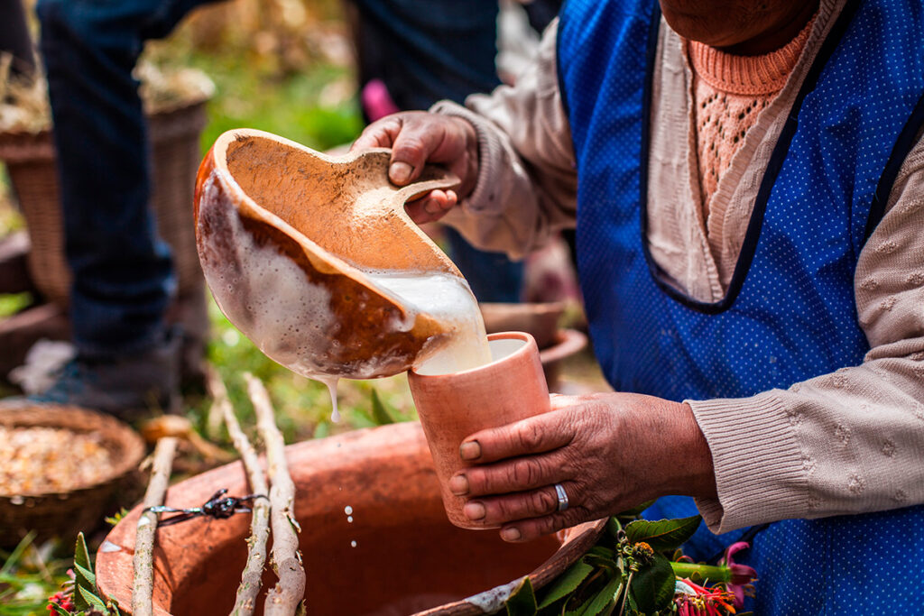 Mujer andina sirviendo chicha de jora en una jarra de barro, en un entorno rural del Cusco