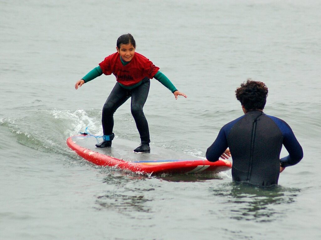 Clase de surf para principiantes en Huanchaco, con instructor acompañando en aguas tranquilas
