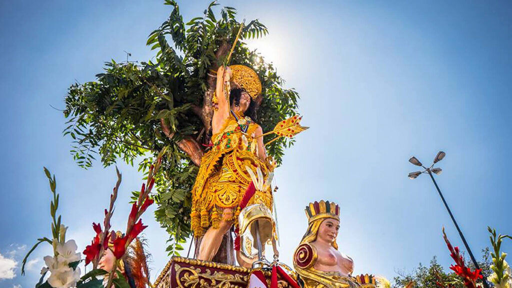 Imagen de San Sebastián en procesión en Cusco, ricamente adornada y rodeada de figuras simbólicas andinas bajo un cielo despejado
