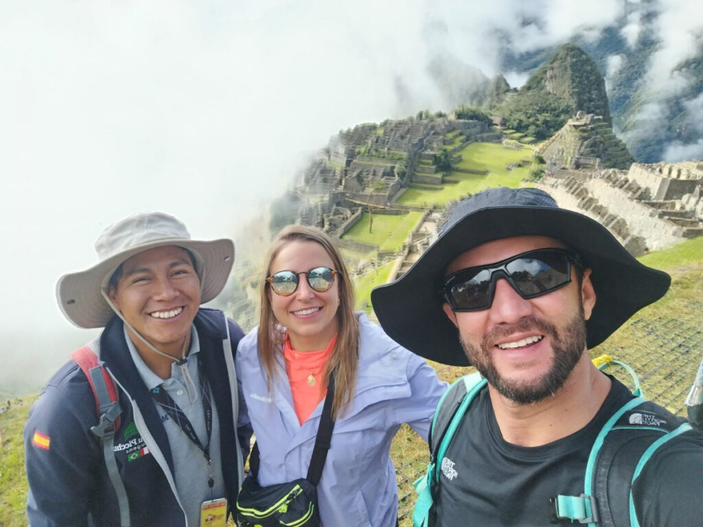 Guía turístico de Viagens Machu Picchu junto a turistas durante su visita a la ciudadela inca, con vista panorámica de las ruinas y las montañas andinas