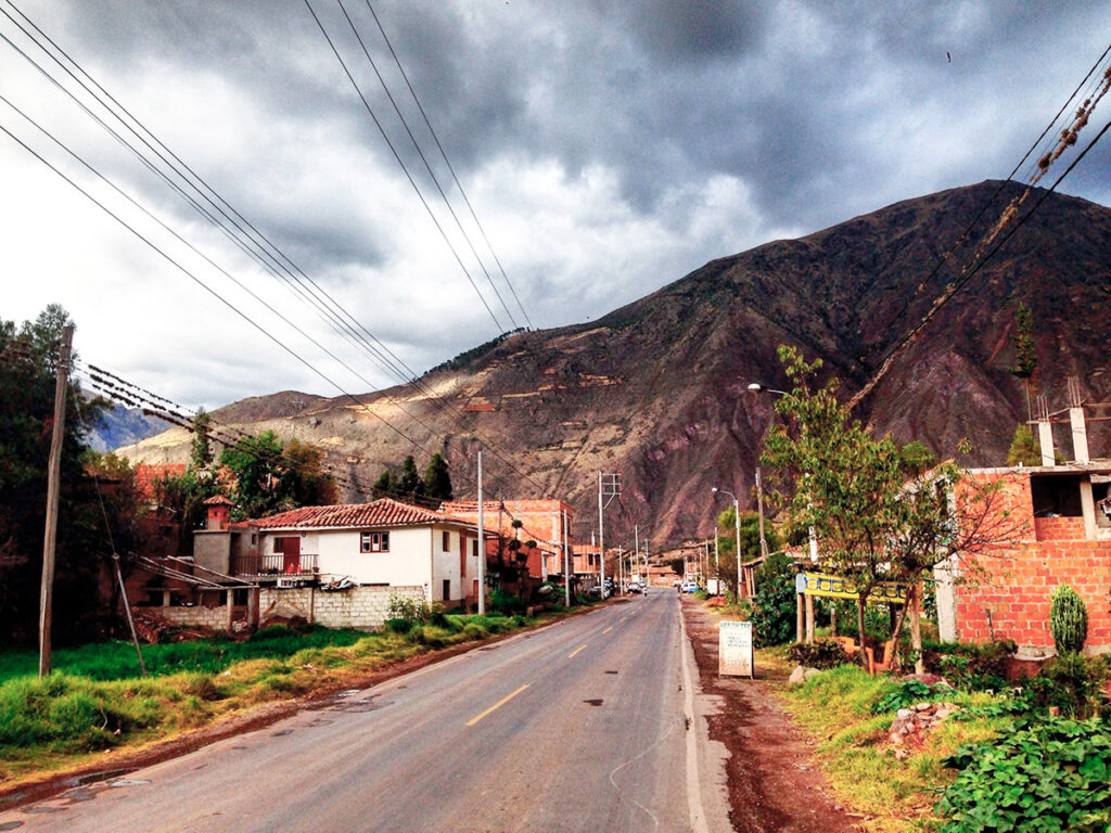 Calle principal de Huayllabamba con casas tradicionales, postes eléctricos y montañas andinas al fondo