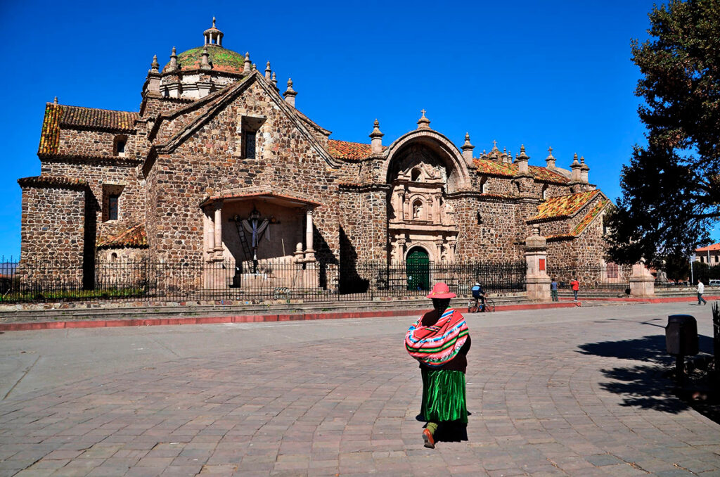 Fachada de piedra rosada de la iglesia de Santiago Apóstol en Lampa, con una mujer en traje típico caminando hacia la entrada