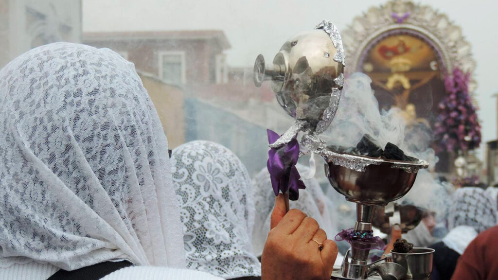 Mujeres con velo blanco en una procesión religiosa sostienen un incensario humeante ante la imagen del Señor de los Milagros