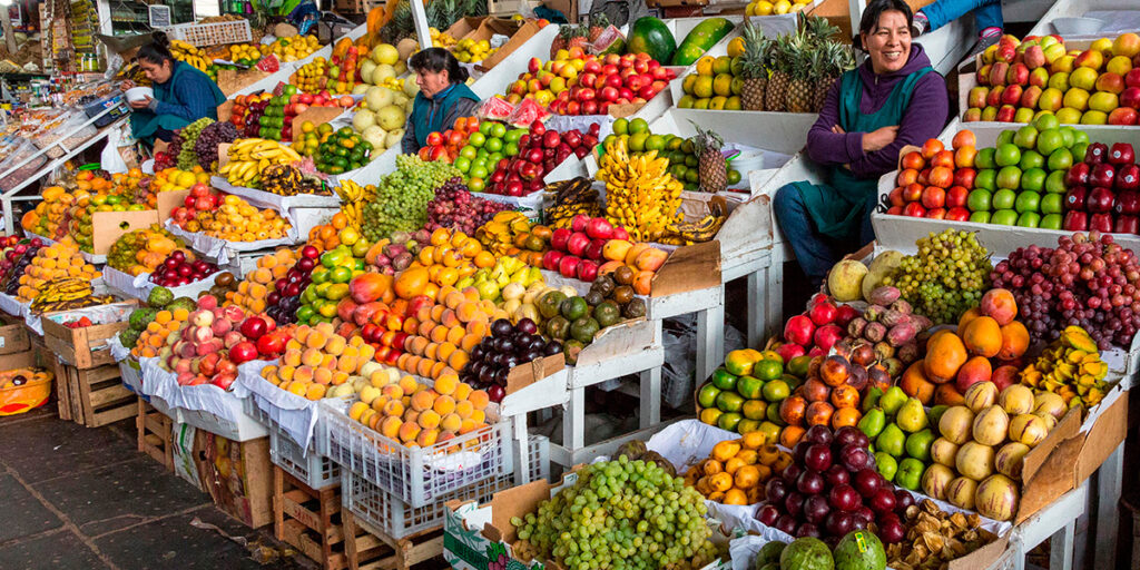 Puestos de frutas coloridas en un mercado peruano, atendidos por comerciantes sonrientes