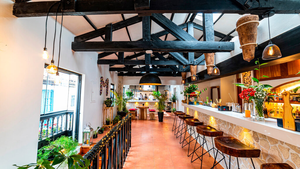 Interior del restaurante Morena Peruvian Kitchen en Cusco, con decoración moderna, techos altos de madera y una barra iluminada junto a plantas ornamentales