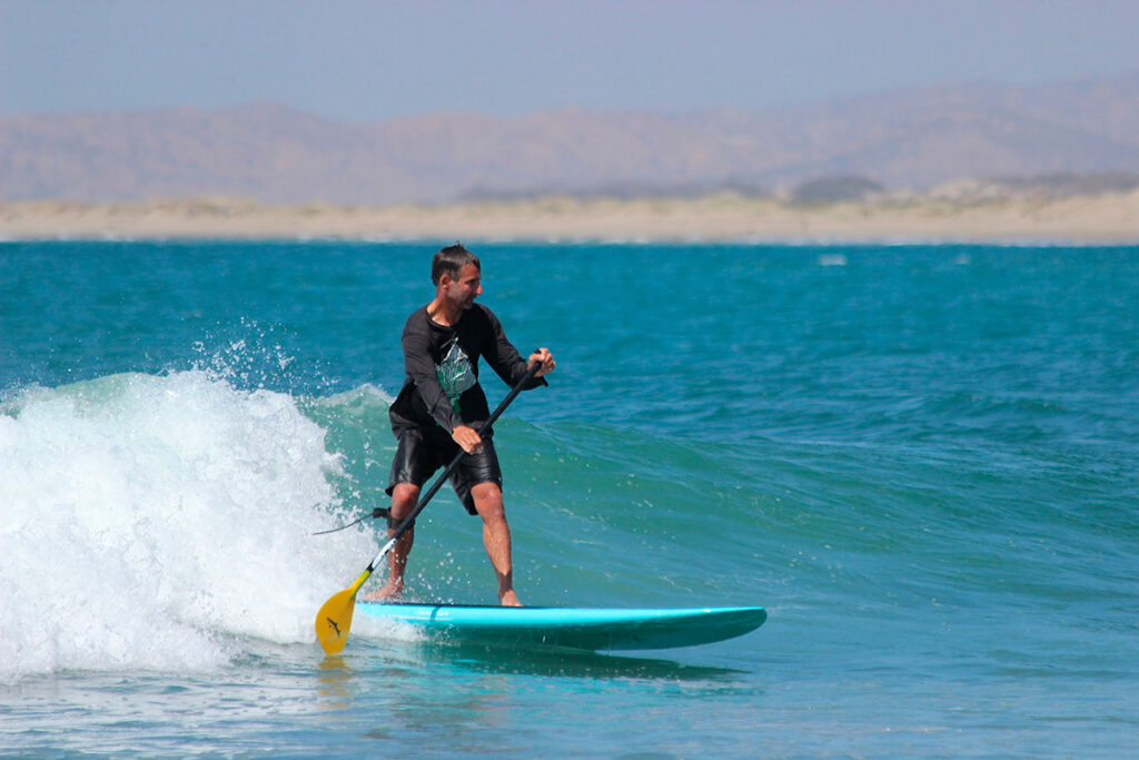Persona practicando paddle surf sobre una ola en la playa de Máncora, norte del Perú