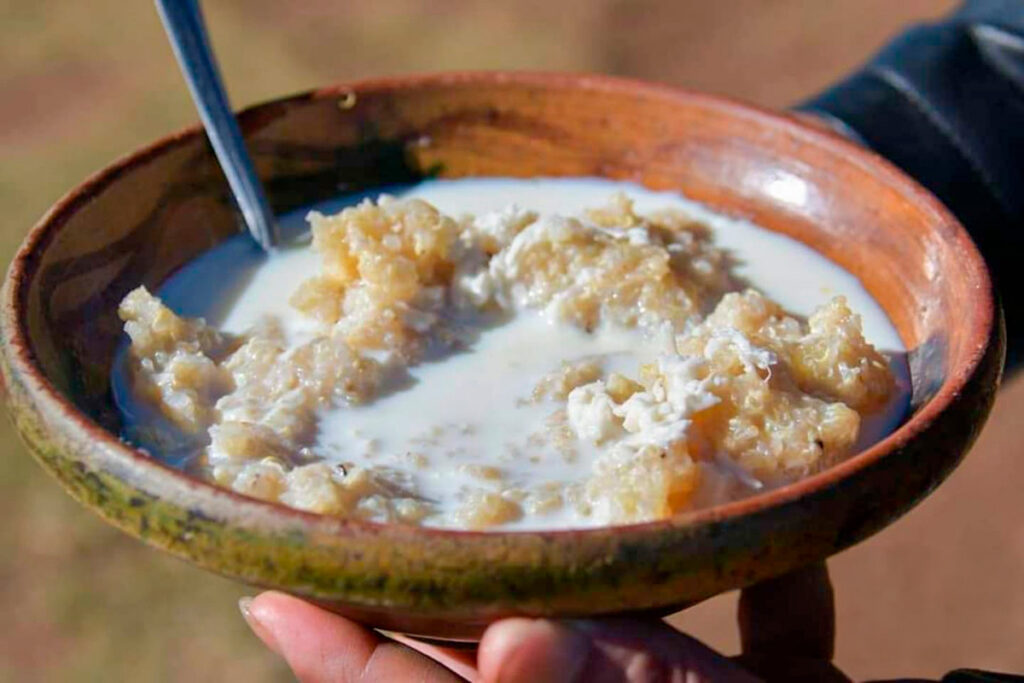 Pesque de quinua servido en un cuenco de barro, con leche y una cuchara de metal