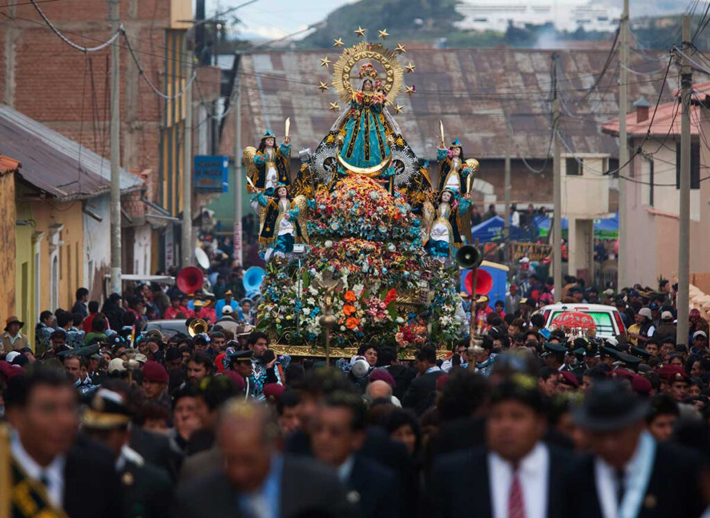 Procesión multitudinaria de la Virgen de la Candelaria recorriendo una calle de Puno, con arreglos florales, músicos y fieles acompañando la imagen