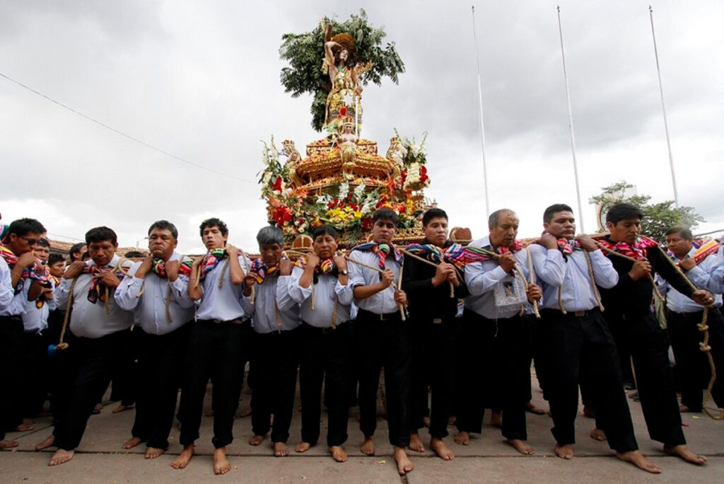 Fieles cargando la imagen de San Sebastián en andas durante una procesión en Cusco, descalzos y con vestimenta formal, en un acto de devoción colectiva
