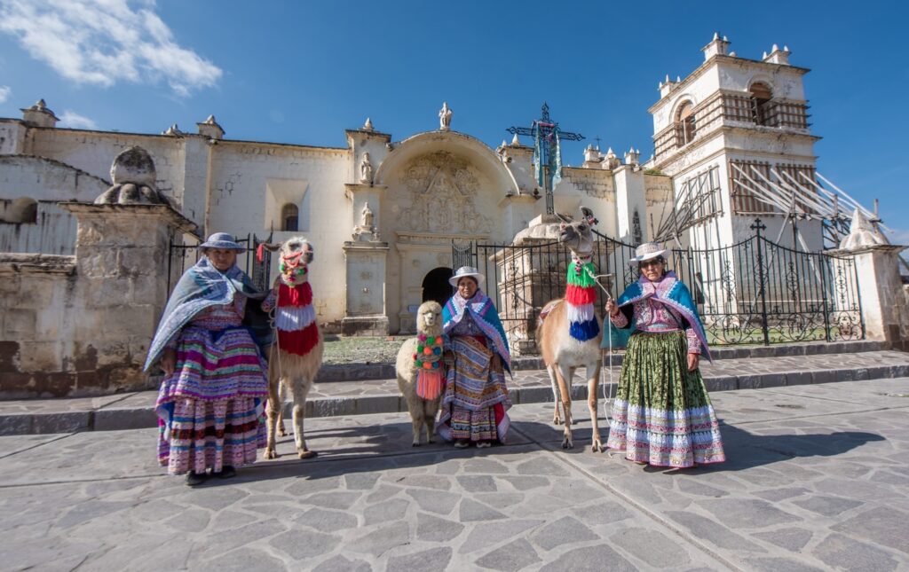Mujeres con trajes típicos collaguas y llamas frente a la iglesia de la Inmaculada Concepción en Yanque, Valle del Colca