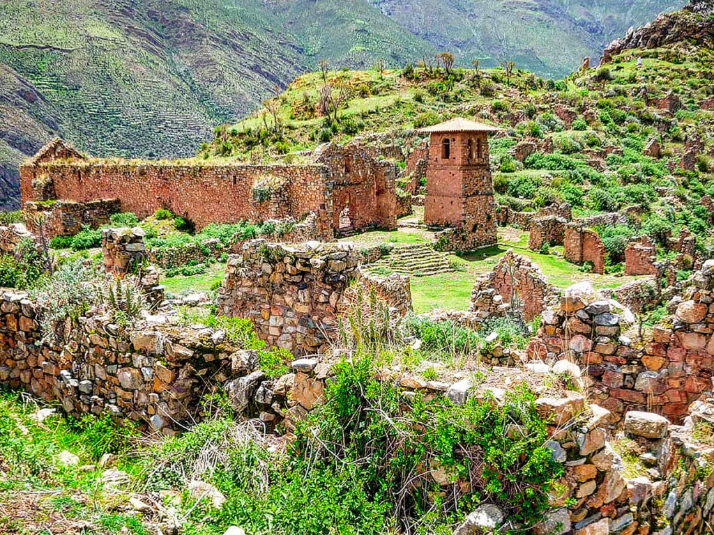 Vista parcial del sitio arqueológico de Pumamarka, con recintos de piedra rodeados de vegetación andina y montañas al fondo