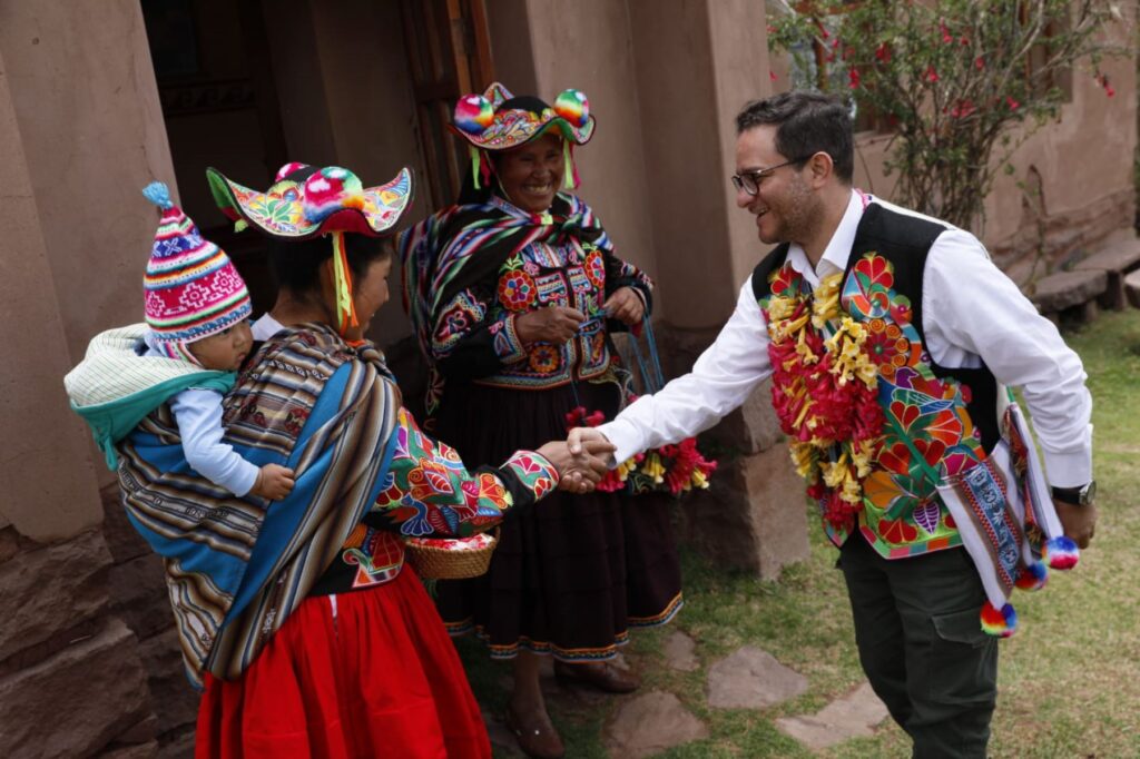 Mujeres andinas con vestimenta tradicional reciben a un visitante con un apretón de manos en un contexto de turismo comunitario