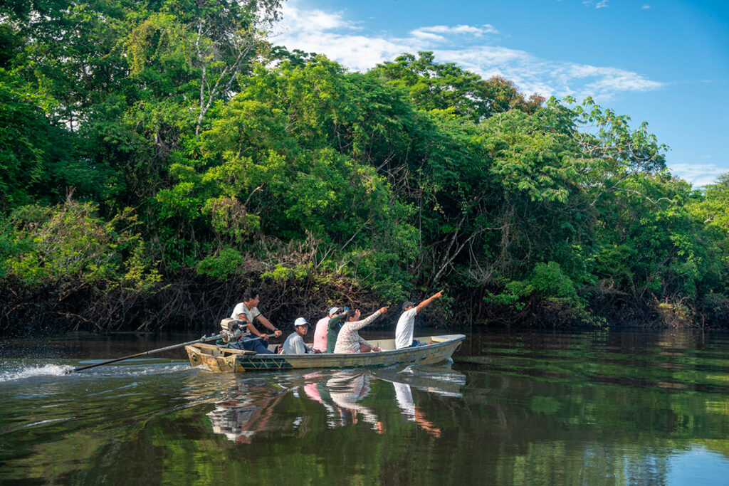 Turistas y guía local navegan en bote por un río de la Amazonía, rodeados de densa vegetación y cielos despejados