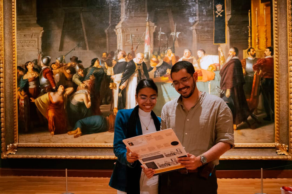 Pareja observando una guía durante su visita al Museo de Arte de Lima (MALI), con una pintura histórica de fondo