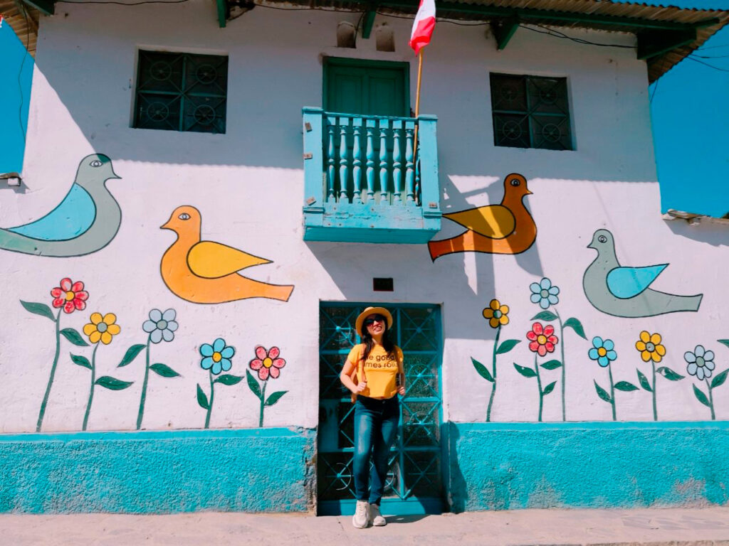 Mujer frente a casa decorada con aves y flores en estilo naïf en el distrito de Antioquía, Lima región