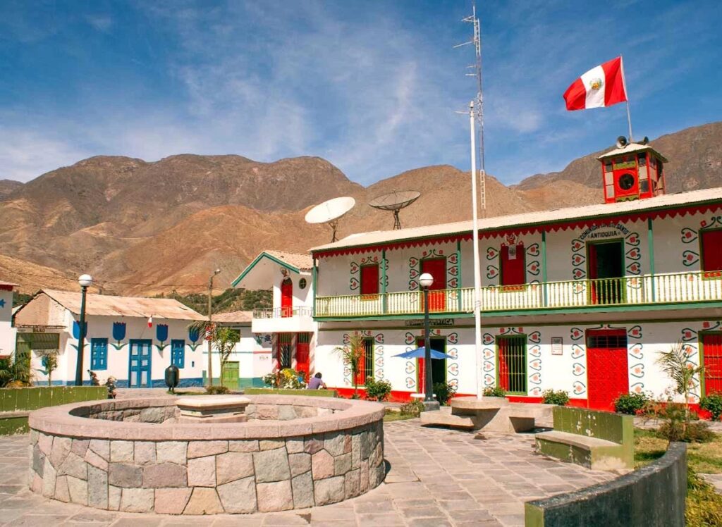 Plaza principal de Antioquía con fachadas decoradas en estilo naïf y bandera del Perú al viento