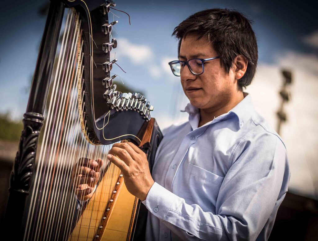 Músico andino tocando arpa tradicional durante la interpretación de un huayno