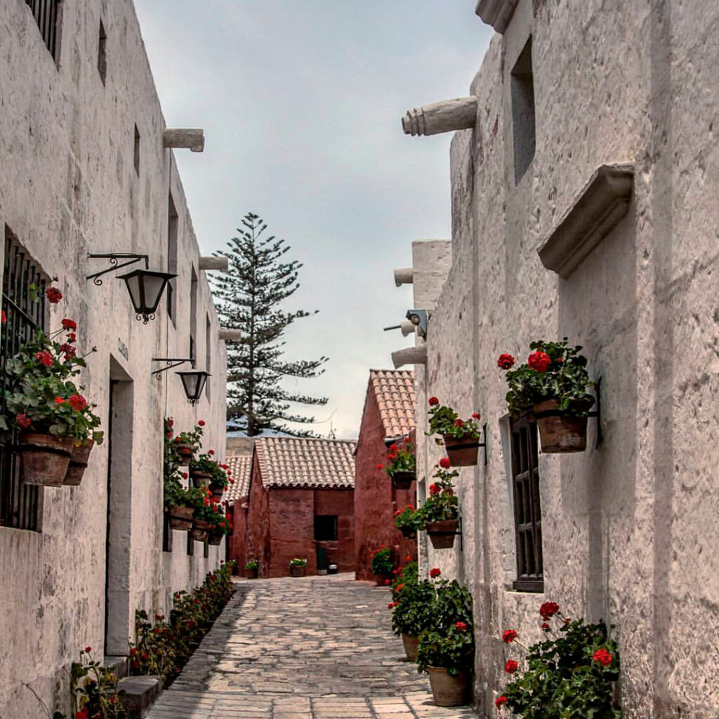 Calle interna de la Casa Tristán del Pozo en Arequipa, con muros de sillar blanco, flores en balcones y piso empedrado