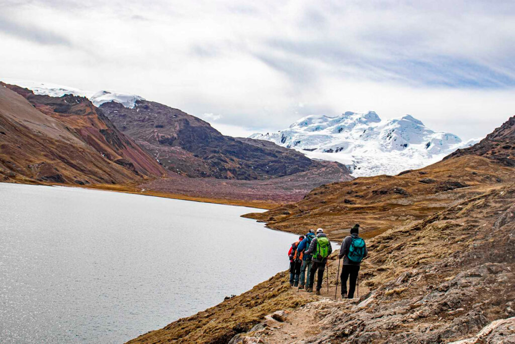 Excursionistas caminando junto a una laguna altoandina en la cordillera Vilcanota, con glaciares en retroceso al fondo